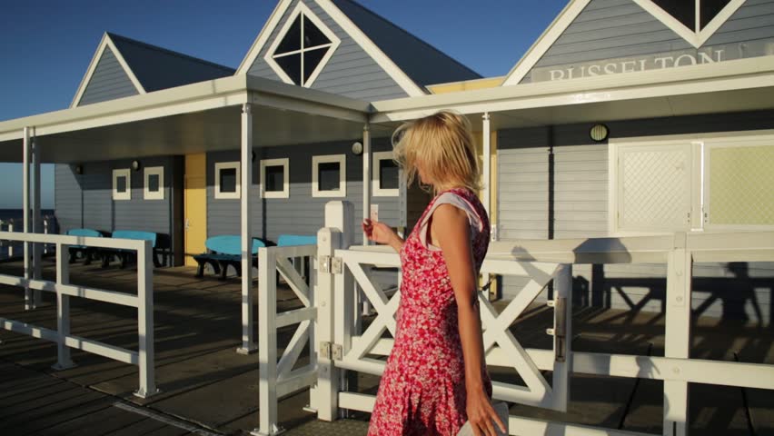 Blonde caucasian woman walking at famous Busselton wooden jetty in Busselton, Western Australia with sunset light. Female tourist in iconic place. Summer and holidays season.
