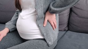 Close up side view of young pregnant woman massaging back muscles sitting on sofa, suffering from severe painful feelings, female 20s  with third trimester big belly having joints strain in lower back - Powered by Shutterstock - Get 15% off with code: PIKWIZARD15