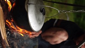 Cooking over a campfire at a campsite. Cooks food in nature at an outdoor camping.The concept of tourism. Tourist information. Hiking lifestyle. Vertical video. Vertical orientation of the video.