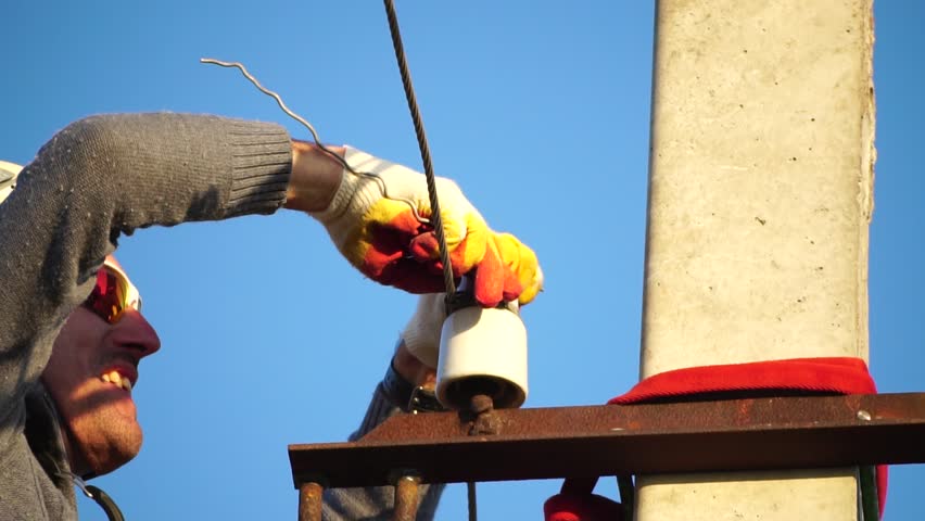 Skilled electrician in helmet fixes wires standing on ladder near high pole against blue sky on summer day backside view. Electrical service and mounting on the pole. Slow motion Royalty-Free Stock Footage #1098416355