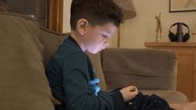 Little boy watching smartphone. Boy on sofa playing with a smartphone. Bright blue light on his face. Boy Watch Television in Evening. Video Game Entertainment Emotions Family. Portrait kid
