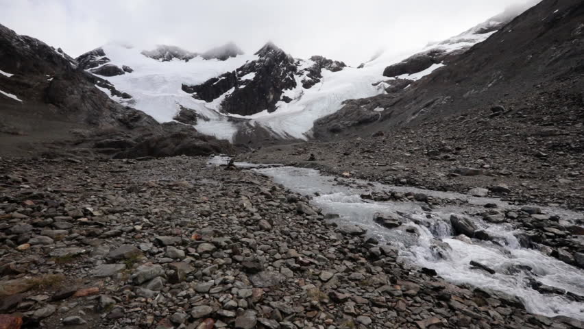 High in the Andes mountains. Environmental. View of Vinciguerra glacier in the rocky mountaintop, the ice field, snow and stream of fresh melting water flowing downhill.