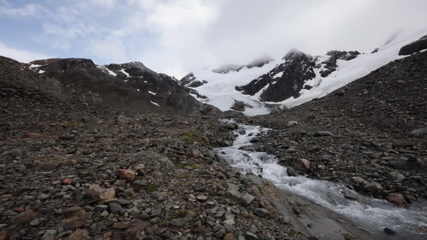 High in the Andes mountains. Environmental. View of Vinciguerra glacier in the rocky mountaintop, the ice field, snow and stream of fresh melting water flowing downhill.