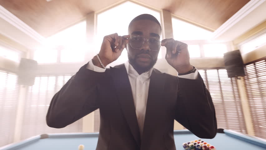 A video of a man looking at the camera while trying to fix his sunglasses and suit