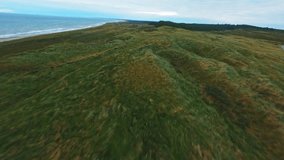 Aerial footage of a drone flying above the rough and grassy terrains of a seaside hill on a cloudy day