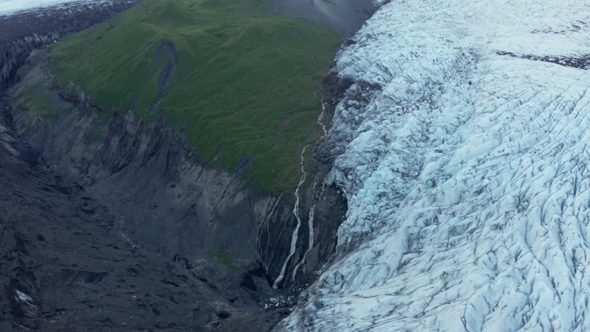 Contrast in landscape between black volcanic mountain and white glacier