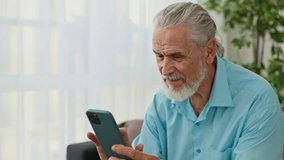 Close view of the happy mature caucasian man sitting on the sofa and using smartphone. Senior male pensioner is chatting on the social media. Technology and communication concept - Powered by Shutterstock - Get 15% off with code: PIKWIZARD15