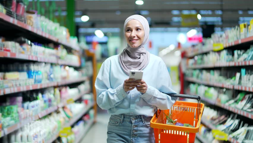 Young muslim woman in hijab Buyer customer checking shopping list using smartphone, purchasing in grocery store in supermarket female shopper pick use mobile phone in hypermarket or food market | Shutterstock HD Video #1098426701