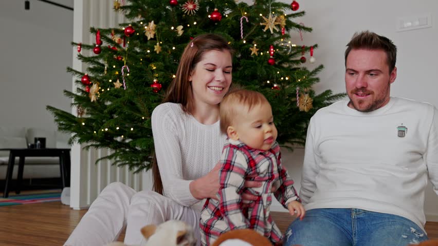 Baby girl crawling away from her parents, sitting under the Christmas tree