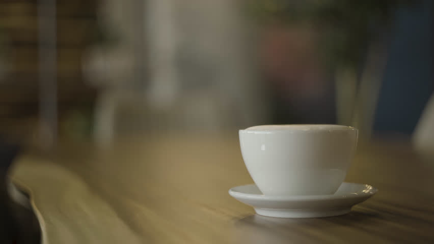Cafe latte in a white mug is placed on a wooden table. | Shutterstock HD Video #1098439211