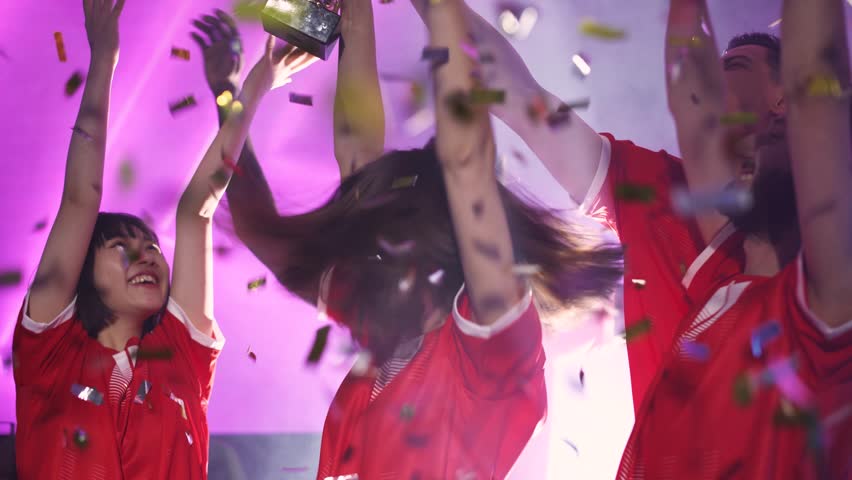 Team victory, group of esports players rejoices at the victory in the international championship, female holds the gold cup in her hands, confetti is flying in the air.