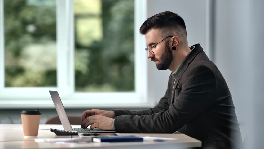 Bearded fashion male skilled manager employee working laptop chatting online desk workplace at office window. Man boss smart handsome entrepreneur cyberspace deal discussing to partner at workspace | Shutterstock HD Video #1098441267