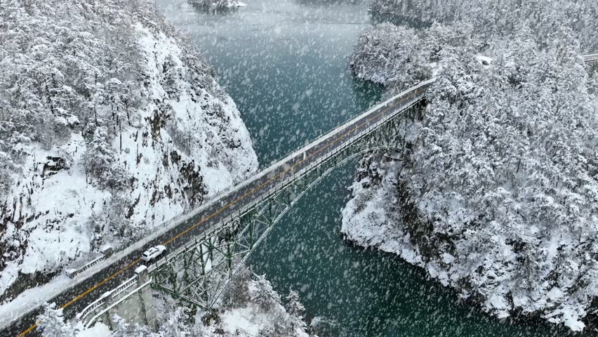 Aerial view of cars driving over Deception Pass while snow is actively falling.