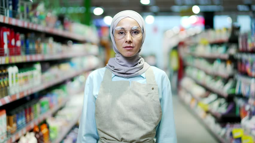 Portrait Muslim woman in hijab worker in supermarket grocery store or deli in apron looking at camera female sales manager small business owner employee in food market hypermarket friendly arm crossed Royalty-Free Stock Footage #1098444131