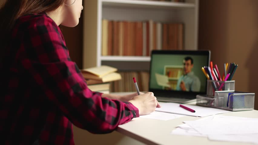 learn virtual. a teenager girl is studying remotely from a teacher online on a laptop sitting at a table next to a bookcase. distance learning education indoor concept. student on exam online Royalty-Free Stock Footage #1098447171