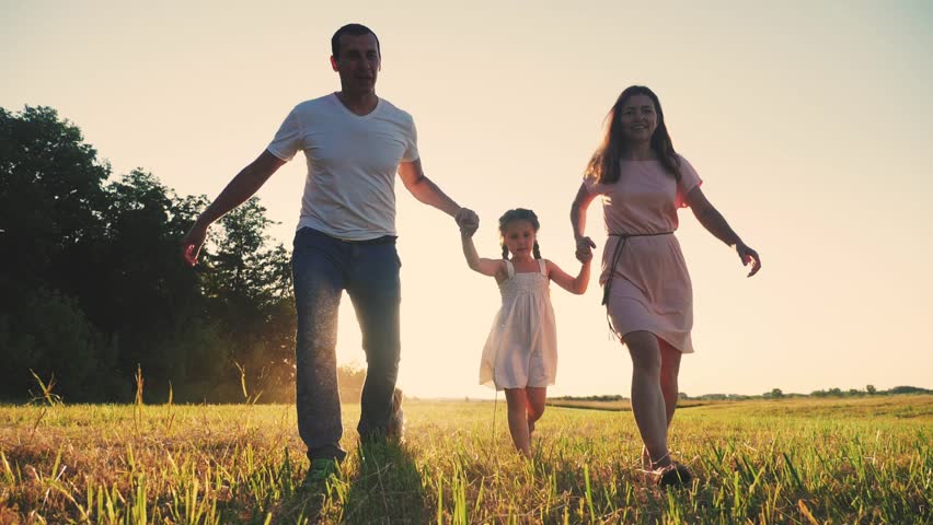 happy family running in the park. dad and mom silhouette throw up their daughter up holding hands run next outdoor to a dog in a park in nature. friendly family running together at sunset back view