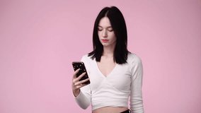 4k slow motion video of cute girl using phone over pink background.