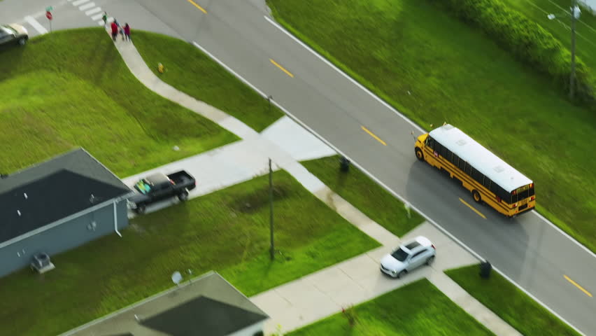 Aerial view of american yellow school bus picking up children at sidewalk bus stop for their lessongs in early morning. Public transportation in the USA | Shutterstock HD Video #1098448989