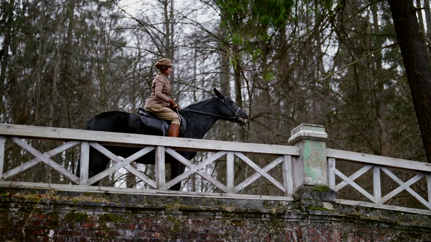 elegant lady in vintage jockey suit riding black stallion in royal garden, moving on old bridge