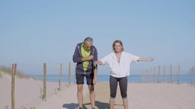 Focused elderly couple exercising on sandy beach on summer day. Front view of man and woman cooling down after intense outdoor workout, bending to sides, raising arms up. Sport, family concept - Powered by Shutterstock - Get 15% off with code: PIKWIZARD15