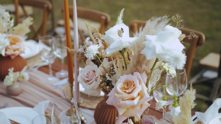 Close-up beautiful bouquet of roses and dried flowers on the table served and decorated with candles in boho style wedding dinner, plates and wine glasses, no people shot, slow motion. Royalty-Free Stock Footage #1098454613