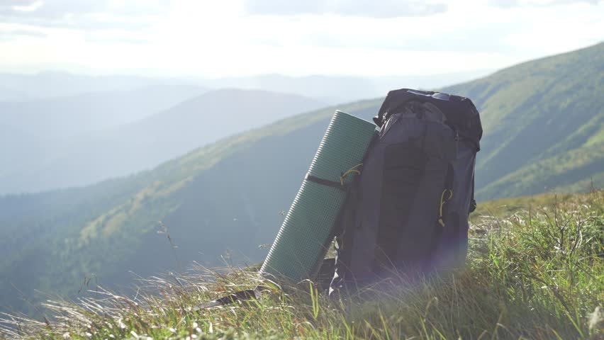 A backpack on the grass on a sunny day, a man picks it up and leaves. Backpack close-up. Mountain landscape, a tourist lifts a backpack and continues the hike. High quality 4k footage