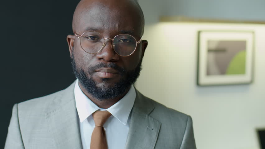 Chest up portrait shot of African American businessman in formal suit and eyeglasses standing in office and posing for camera | Shutterstock HD Video #1098457347