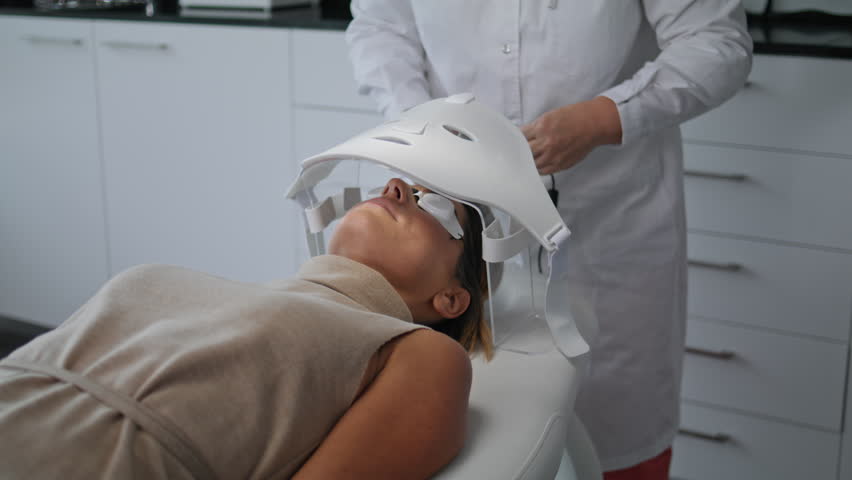 Unknown cosmetologist doing skin treatment turning on special led mask for phototherapy close up. Woman client lying under modern phototherapy equipment for wrinkles correction. Beauty clinic concept. Royalty-Free Stock Footage #1098459263