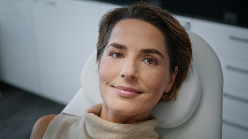 Cosmetology client looking camera lying on medical chair modern clinic close up. Portrait of attractive woman waiting for dermatologist cosmetologist consultation. Beauty salon patient relax smiling. Royalty-Free Stock Footage #1098459339