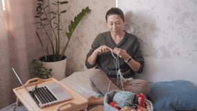 Close-up video of woman crocheting something. Anti-stress hobby. Tranquil leisure at home. Handicraft. Online lessons for amateurs on laptop.