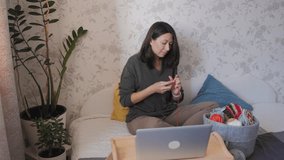 Close-up video of woman knitting something small. Anti-stress hobby. Tranquil leisure at home. Handicraft. Online lessons for amateurs on laptop.
