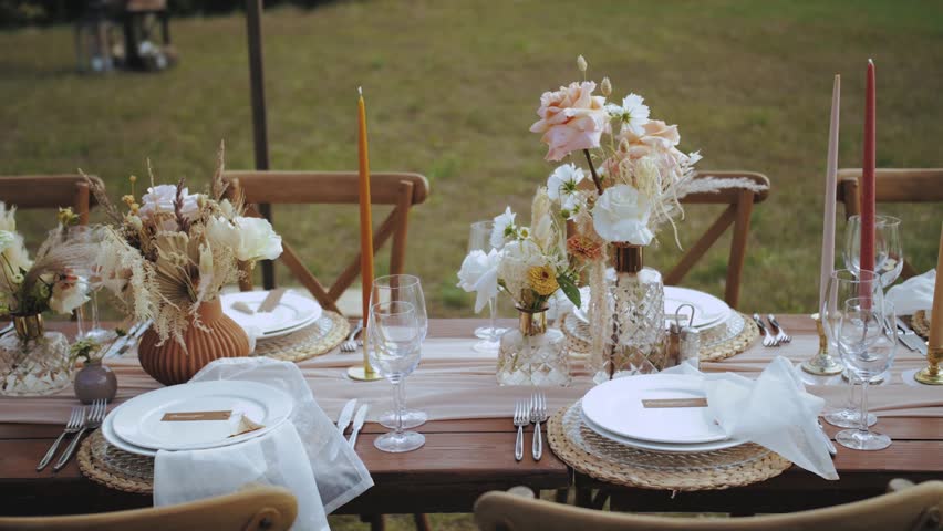 Close-up table served and decorated with candles and dried and pastel flowers for boho style wedding dinner, plates and wne glasses, no people shot, slow motion. | Shutterstock HD Video #1098477661