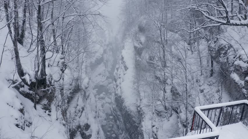 Going up aerial shot of Urukh river canyon and the road running alongside at winter snowfall. Digoria, North Ossetia, Russia.