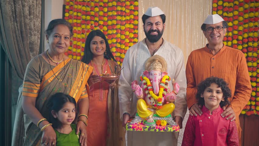 Happy ethnic Hindu Indian young man holding a Ganapati idol with smiling family members in traditional clothes looking at the camera during Ganesha Chaturthi festival or celebration in decorated house Royalty-Free Stock Footage #1098496315