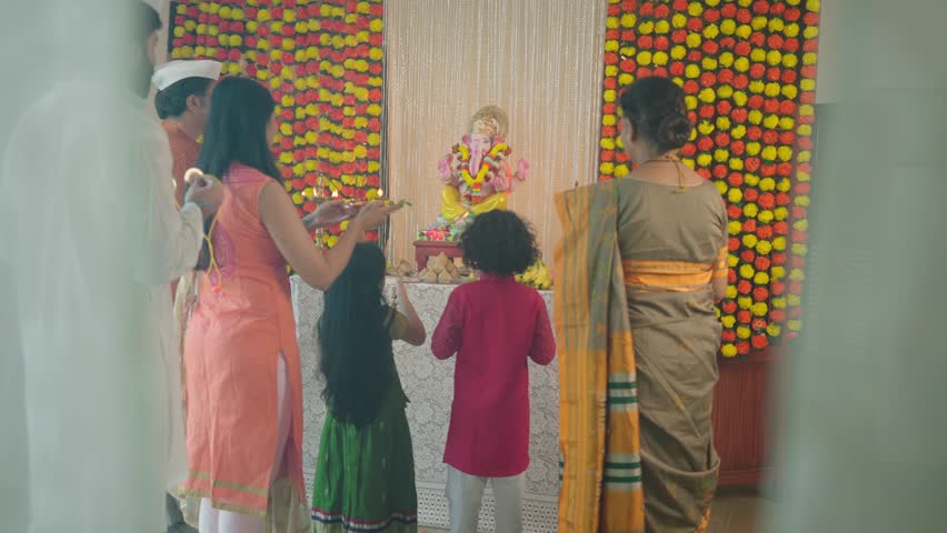 Happy ethnic Hindu Indian family offering a prayer called Aarti to the Ganapati idol decorated with marigold flowers during the Ganesha Chaturthi festival or celebration in an indoor house Royalty-Free Stock Footage #1098496317