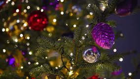 Close-up view of glass purple cone shaped bauble hanging on Christmas tree on night city square. Real time video. Selective focus. Winter holidays theme.