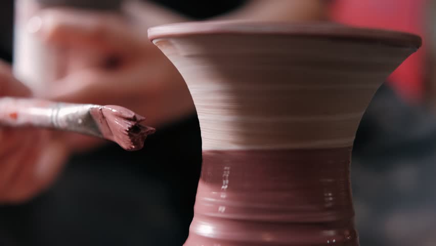 Female potter paints on rotating clay pot on the pottery wheel. Close up shot of potter making ceramic pot on pottery wheel at workshop, slow motion. Creativity and traditional crafts concept. Royalty-Free Stock Footage #1098509369