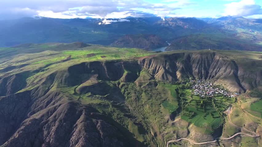 Aerial view of flat farmland on high plateau above mountains and village.