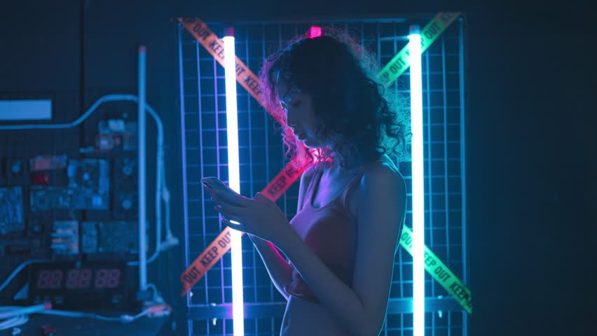 Young Asian teenage women using smart phone in a room filled with blue and pink neon lights.