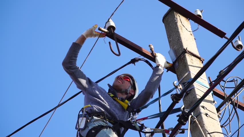 Skilled electrician in helmet fixes wires standing on ladder near high pole against blue sky on summer day backside view. Electrical service and mounting on the pole. Slow motion Royalty-Free Stock Footage #1098516593