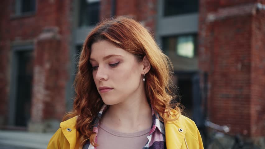 Close-up view of good-looking serious young woman with ginger hair looking at camera. Portrait of calm redhead girl with green eyes on blurred background outdoor. Pensive expression | Shutterstock HD Video #1098517087