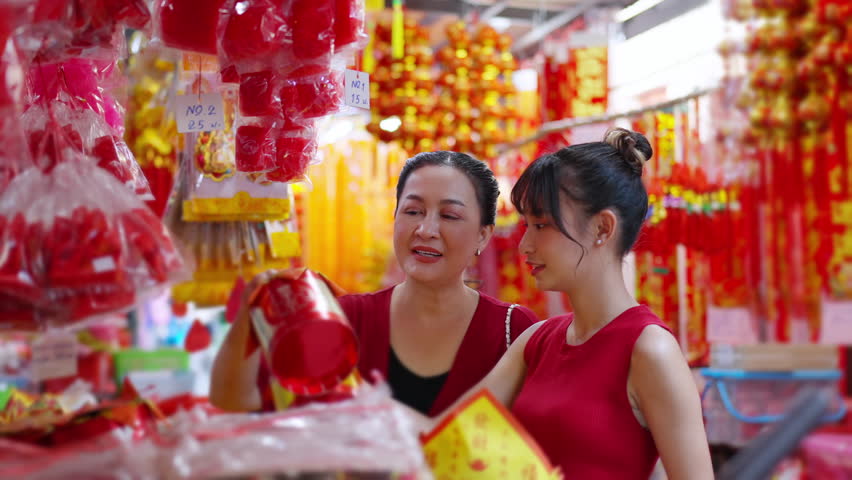 Happy Asian family celebration Chinese lunar new year festival together. Mother and daughter in red blouse holding shopping bag walking and buying home decorative ornaments at Chinatown street market.