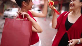 Happy Asian family mother and daughter walking with holding red shopping bag during buying home decorative ornaments for celebrating Chinese Lunar New Year festival together at Chinatown street market