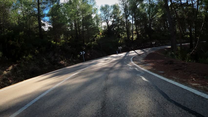 Driving through empty mountain curvy hilly road. Riding fast on new asphalt road through forest and hills. Driving down winding highway surrounded by green trees in sunshine, POV shot.