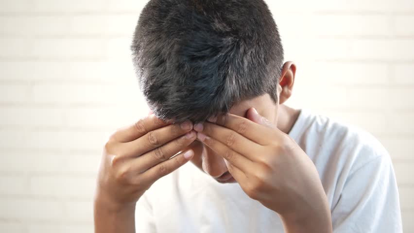 sad teenage boy covering his face sitting on sofa 