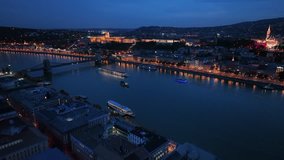 Aerial drone night dolly shot of river cruise ships, Castle Hill, Buda Castle, Gellért Hill and the Citadella with the Danube river, bridges illuminated after sunset in Budapest, Hungary