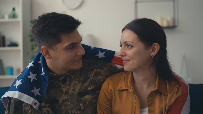 Portrait of American soldier and wife hugging with national flag, family reunion