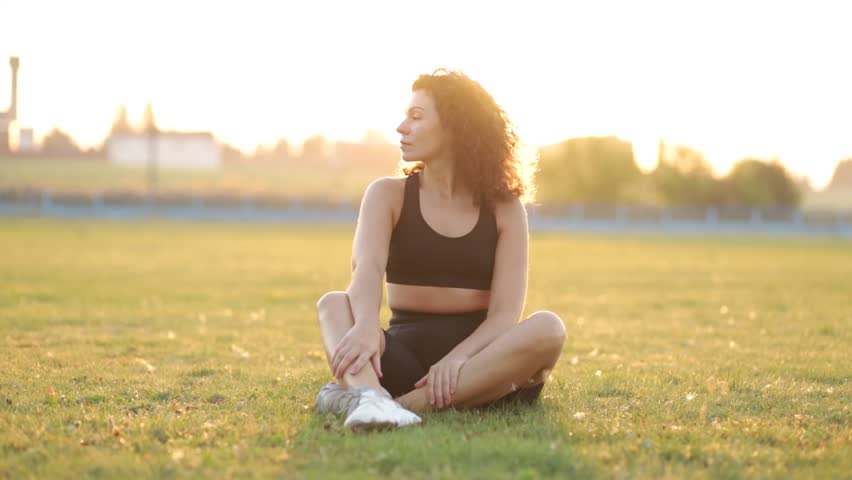 Curly woman goes in for sports yoga gymnastics on a gymnastic mat in the summer on the grass at sunset.	 | Shutterstock HD Video #1098523753