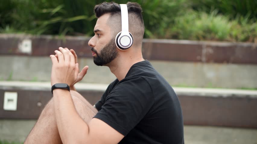 Side view of man doing abdominal crunches with white headphone. Close up of fit guy working abs in park.