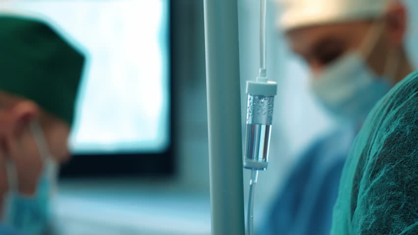 Surgeons in the operating room perform an operation on a patient. A complex surgical operation, a dropper on the background of a surgical operation | Shutterstock HD Video #1098527787